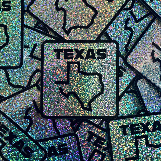 A sticker with a map outline of Texas with bold text 'Texas' on top of it, surrounded by a glittery background.