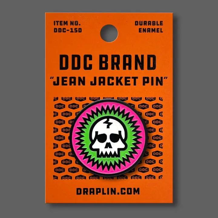 Draplin Design Company skull enamel pin with pink and green burst design on orange backing card